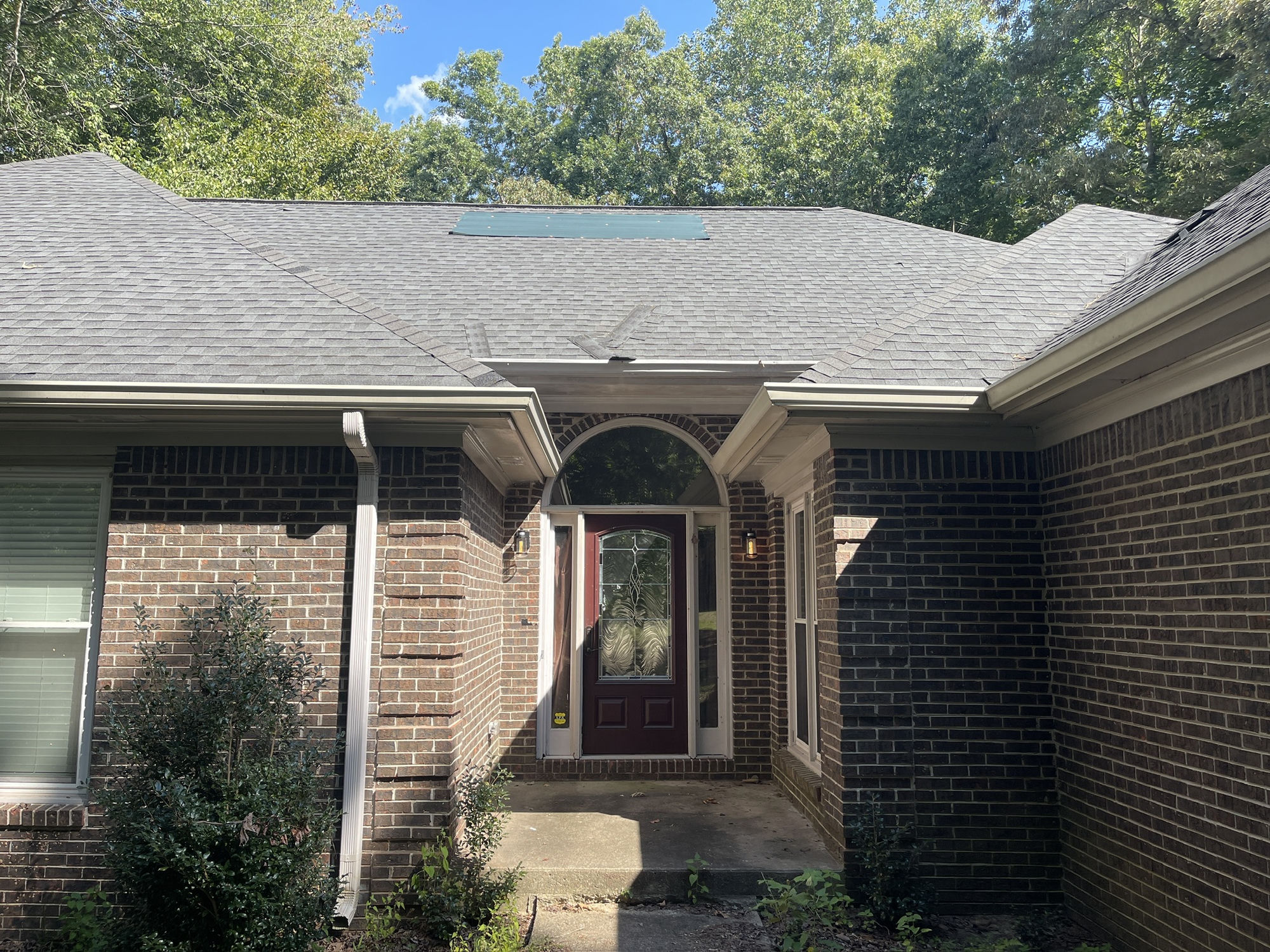 Front entry, wider view. Green tarp patch above the door and torn shingle sections on the adjoining slope to the right.