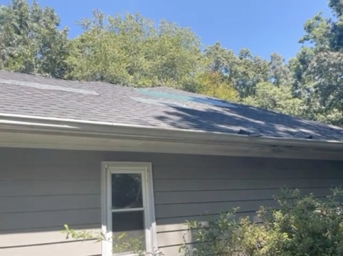 Side elevation. Shingle loss and exposed area near the ridge above the window, visible from ground level.